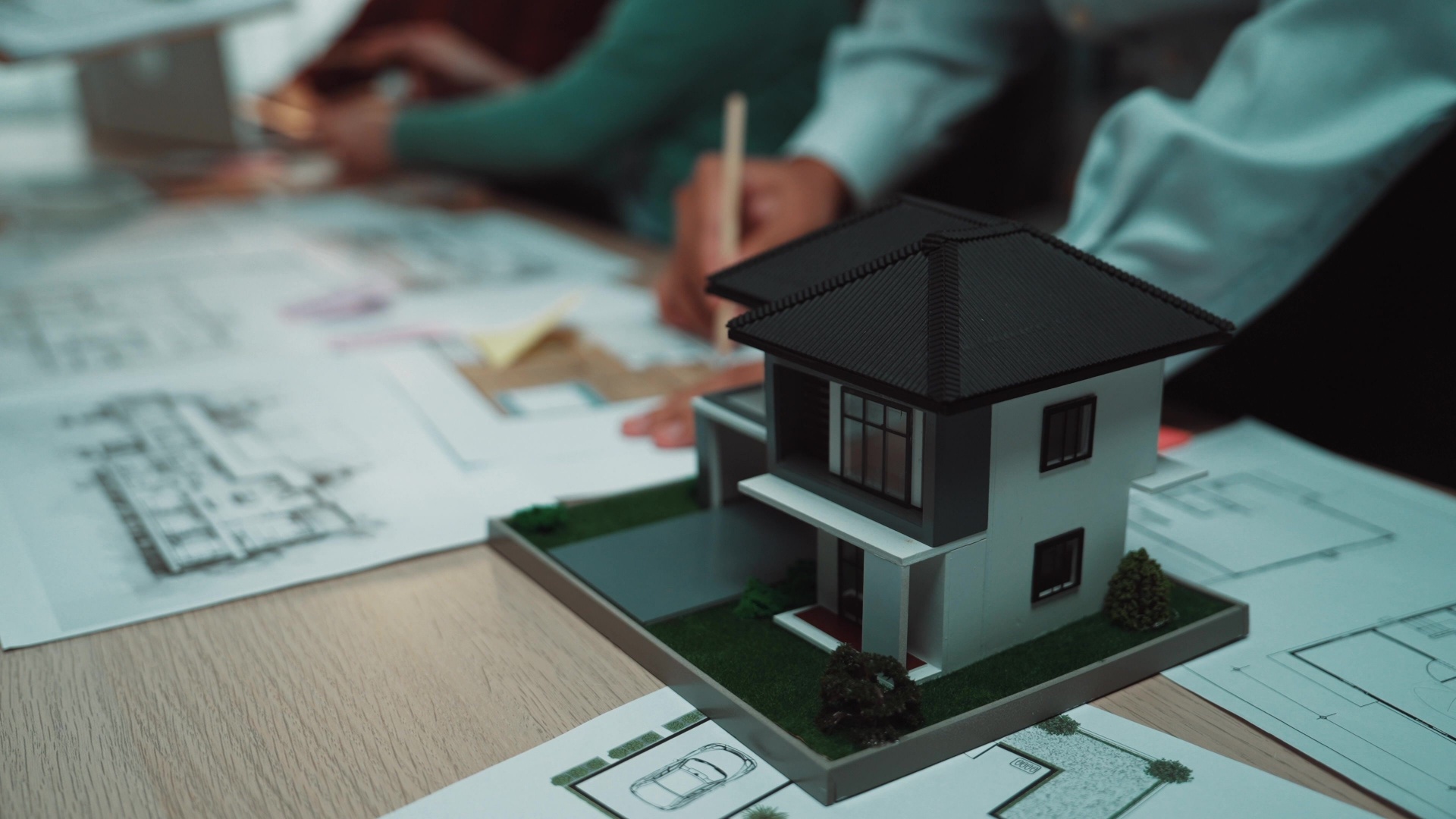 Entreprenører samarbeider om et byggprosjekt. Modell av et hus i fokus som står over byggetegninger